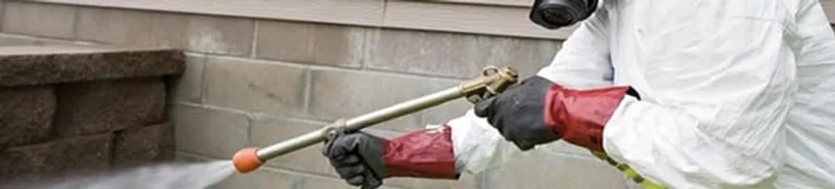 Pest control technician applying exterior insect treatment along a home foundation in Pasadena, CA