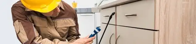 Roach exterminator applying treatment under kitchen cabinets in Pasadena, CA