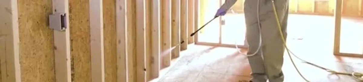 Termite treatment technician applying spray along framing and unfinished walls in Pasadena, CA