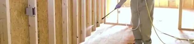 Termite treatment technician applying spray along framing and unfinished walls in Pasadena, CA